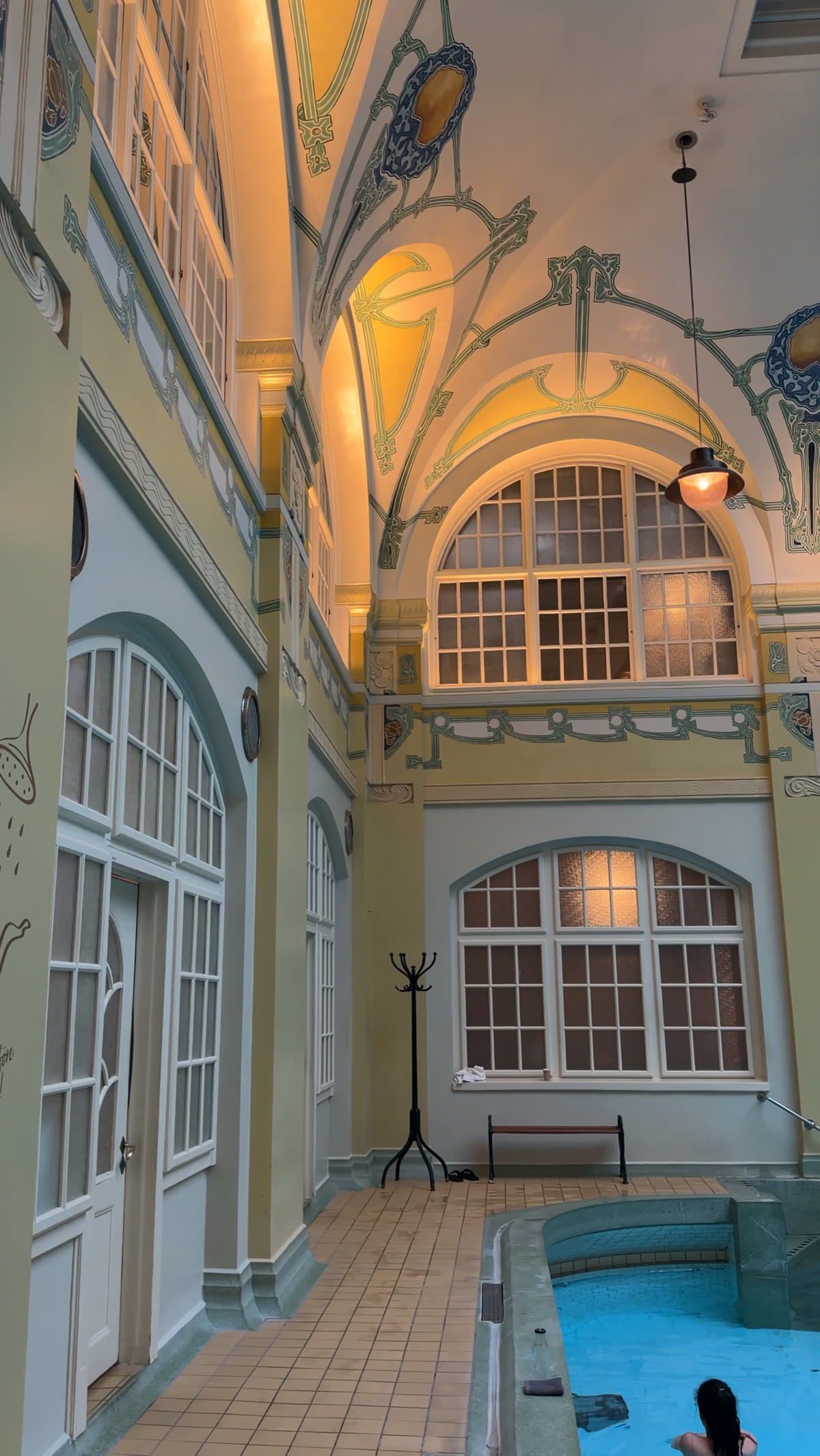 Pale green stairwell with tall arched windows and a painted frieze