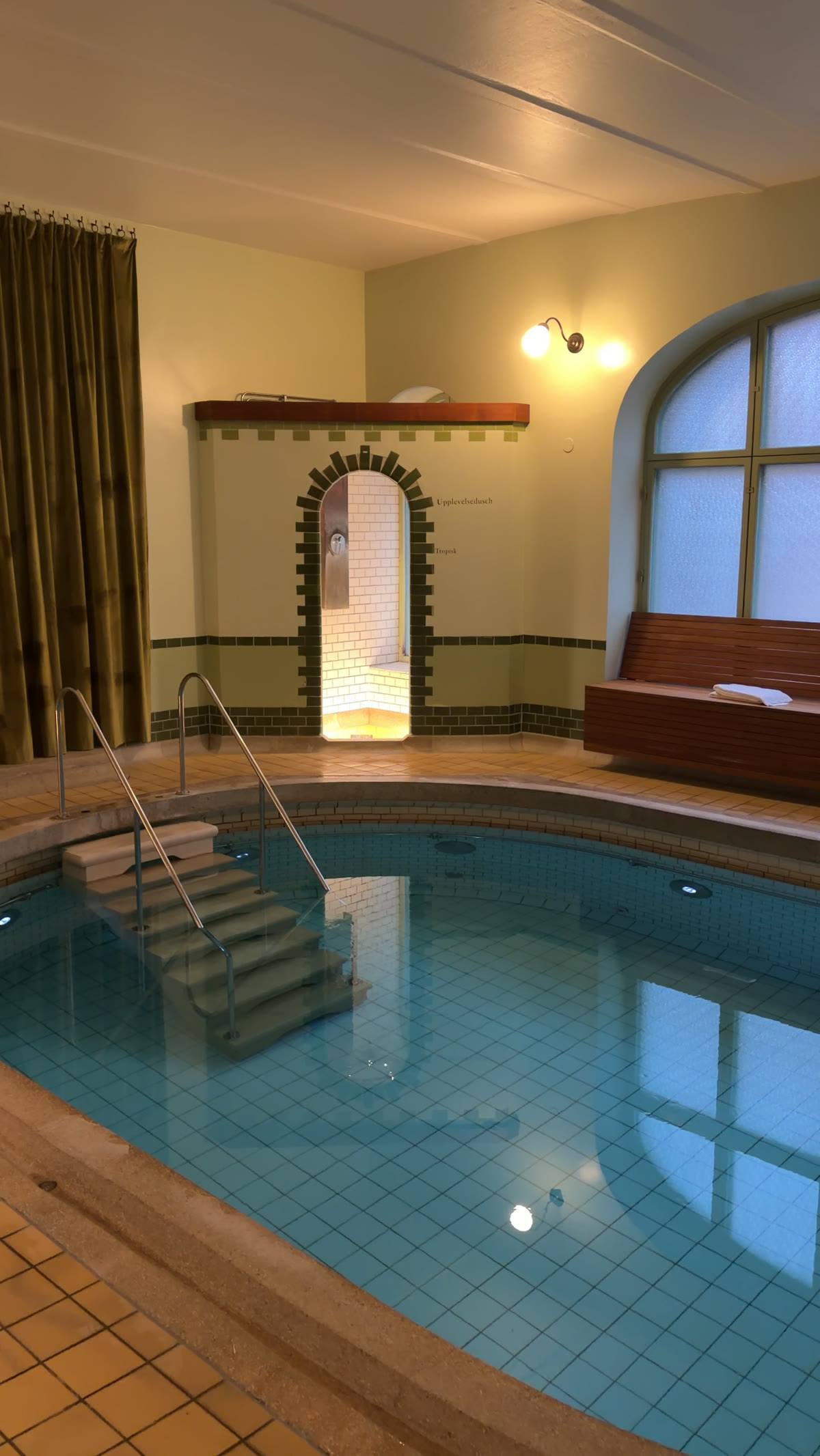 Art Nouveau indoor pool with teal tiles and a lit archway