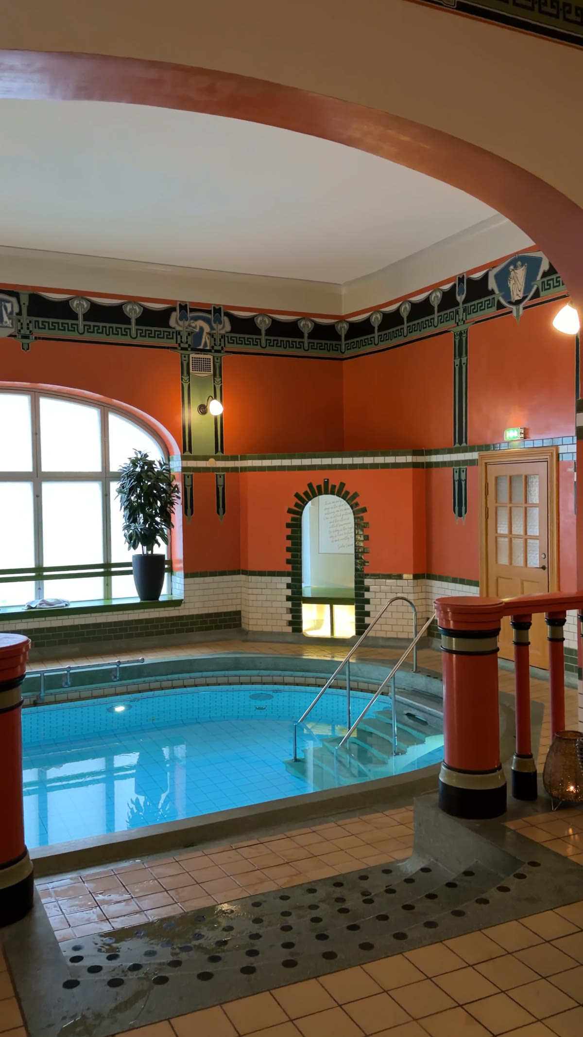 Terracotta pool room with an arched window and brass rails