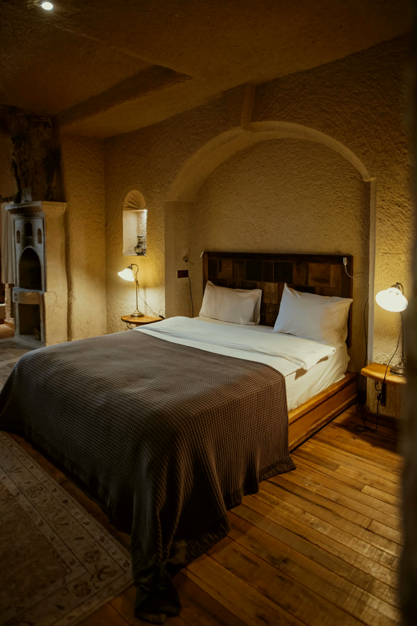 Wood-floored bedroom with a brown throw and warm lamps